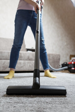 house cleaning concept. a close-up photo of a girl's legs and a vacuum cleaner brush. the girl cleans the house and vacuums the carpet.