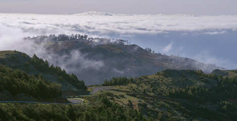 Fog ascending from a valley and remaining among mountain folds. Mountains slopes with mist above trees. Heavy clouds above the Atlantic ocean. Vacation in the Madeira Island.