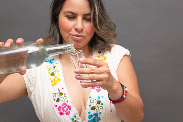 sexy mexican woman in traditional mexican clothes serving shot of silver tequila or mezcal