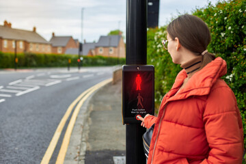 A woman crosses the road by pressing a button at a pedestrian traffic light. A new generation of traffic lights. The concept of a safe city. Traffic rules for children.