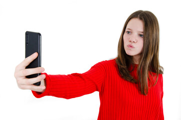 Fototapeta premium Smiling young girl making selfie photo on smartphone. Closeup portrait of beautiful teenage girl making selfie photo on smartphone. Isolated on white background. Close up portrait.