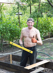 A man of mature years makes high beds on a personal plot. The master works with a level tool to...