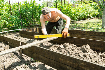 A man of mature years makes high beds on a personal plot. The master works with a level tool to...