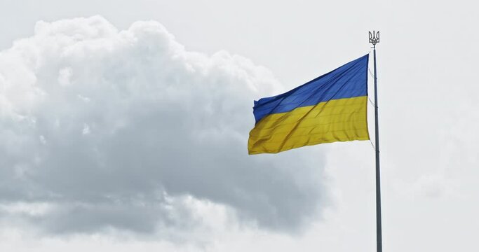 Ukraine flag waving on gray cloudy sky background, 4k footage. Slow motion. Yellow-blue Ukrainian flag with Tryzub coat national country symbol. Copy space for text. Ukraine flag on cloud backdrop