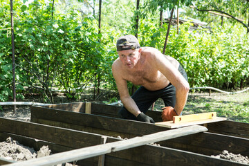 A man of mature years makes high beds on a personal plot. The master works with a level tool to...