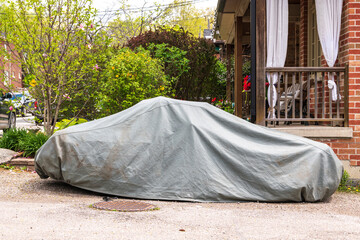 Car cover: a small sports car sits parked on a drive way proctected by a fabric car cover.  Shot in Toronto in spring.