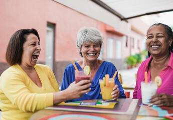 Happy senior female friends having fun together in the city while drinking healthy smoothies at bar outdoor