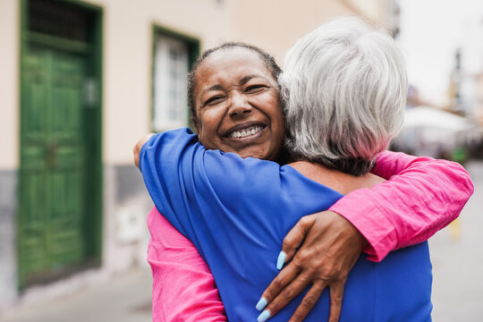 Senior multiracial female friends meeting and hugging each other in the city