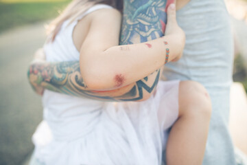 mother with tattoos holds her daughter in her arms, child with peeled elbows hugs mother, close-up