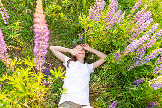 Happy teenage girl smiling outdoor. Beautiful young teen woman resting lying on summer field with blooming wild flowers green background. Free happy kid relaxing and enjoying nature