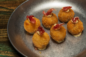 Assortment of ham croquettes on a metal plate topped with a piece of ham