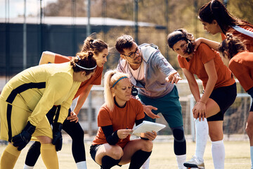 Young coach giving instructions to his female soccer team on playing field.