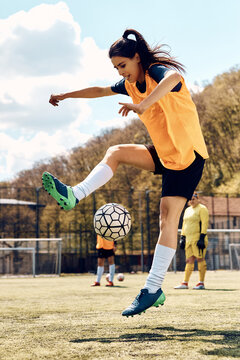 Young woman exercising with ball during soccer training on playing field.