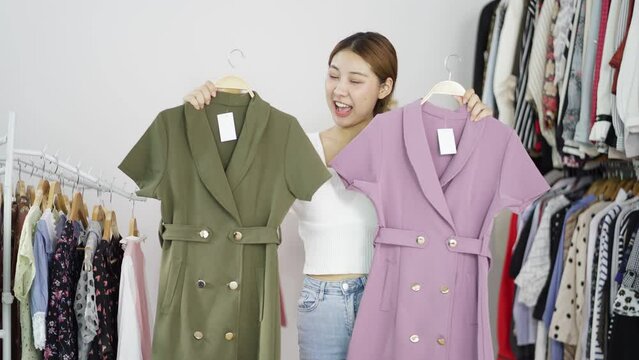 Portrait happy young woman blogger with clothes recording video clip online and talking on camera showing clothes items on hanger rack. Selling product online concept.