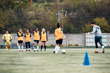 Back view of female soccer player exercising dribbling with ball during sports training.