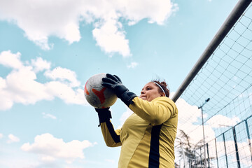 Below view of female goalie catching soccer ball during the match.