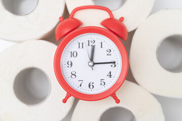 Alarm clock on the toilet paper. The concept of a restroom and problems with long sitting, with constipation. Close up, top view.