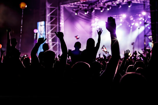 Men and women with raised hands at a concert event.