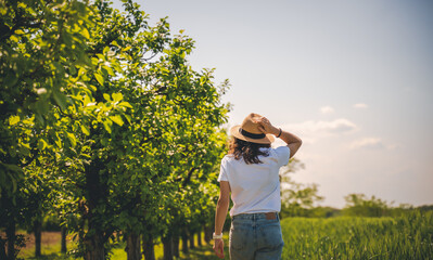 Young woman in a white t-shirt hat and jeans walking in the summer garden