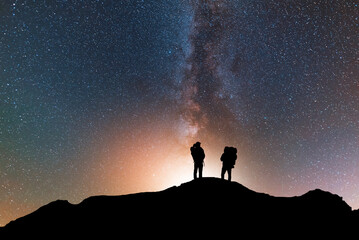 Silhouette of two traveler on the hill in starry night sky.  Bright milky way galaxy behind him. 