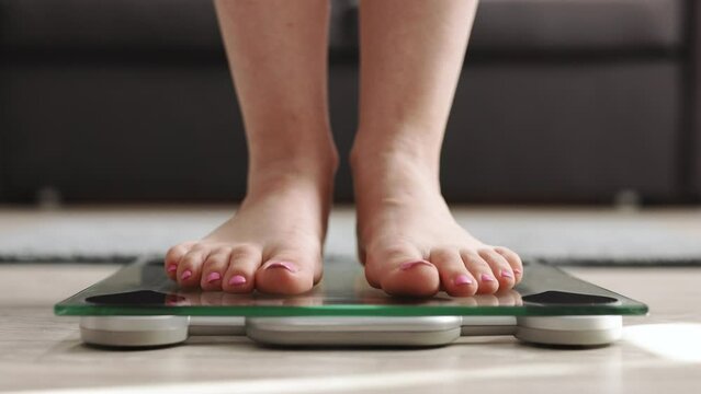 Woman On Scales Measure Weight. Girl Legs Step Bathroom Scale. Fitness Diet Woman Feet Standing Weighing Scales On Room. Barefoot Measuring Body Fat Overweight. Female Dieting Checking BMI Weight Loss