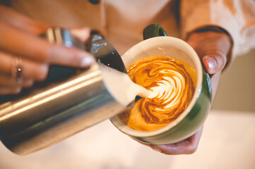 Closeup of hands of a male barista creating pattern and design using cream and utensil on freshly...