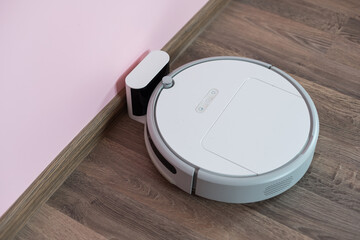 The white robot (robotic) vacuum cleaner is charging on its base. Top view - obrazy, fototapety, plakaty