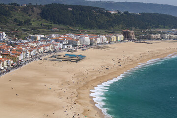 Panoramic view over the beach of Nazaré. On one side we have the ocean on the other the houses and buildings. Nazaré is a very popular surfing destination because of the very high breaking waves. 