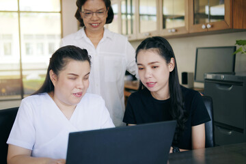  Asian women co-workers in workplace including person with blindness disability using laptop computer with screen reader program for visual impairment people. Disability inclusion at work concepts.