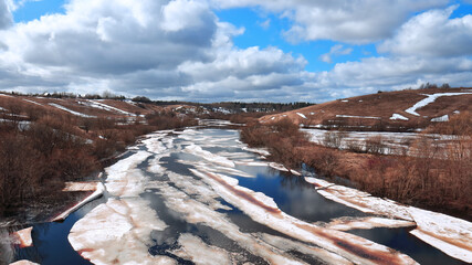 Melting ice on a river in a hilly area under a blue sky with clouds. spring landscape