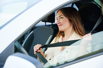 Young happy woman sits at the wheel of a car and hold seat belt looks at window