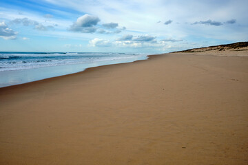 Landscape of a very long sandy beach with a blue sky full of clouds. Horizontal photography.