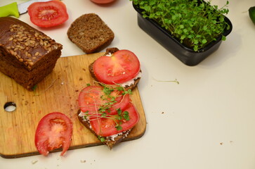 girl cooks and eats for breakfast open sandwich lettuce, tomato, soft cheese. Vegan sandwich with rye bread, spinach, microgreen isolated on white, top view. Healthy eating, diet sandwich closeup