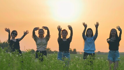 Girls friends waving their hands to the setting sun on the background of the sunset.