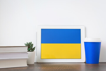 National flag of Ukraine on the tablet, textbooks, a blue cup of hot drink coffee or tea on the...