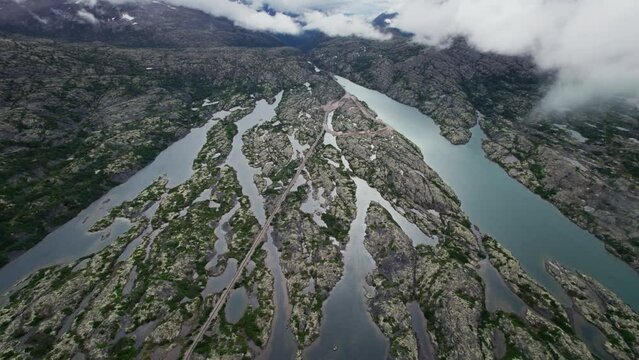 Glacial lake and railway on an igneous rocky mountain valley wth heavy fogs, aerial panoramic shot