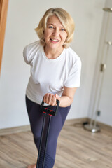 Home training concept. Strong senior woman doing exercises with dumbbells indoors. Cheerful mature lady working out her arm muscles, keeping fit, leading healthy lifestyle