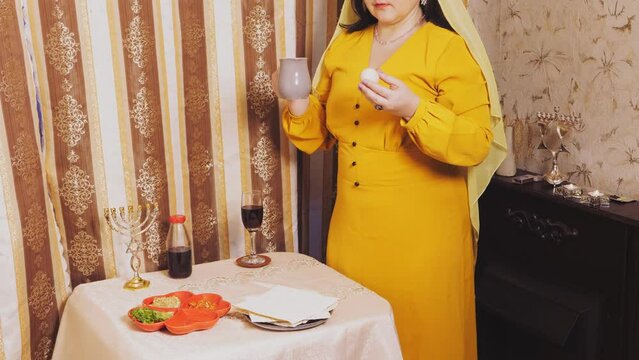 A Jewish woman in a wig and a head veil takes a beitz egg and a jug of salt water in her hand to fulfill the commandment. Overall plan