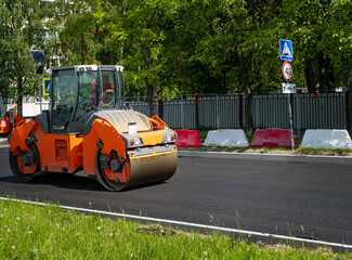 orange steamroller leveling freshly laid asphalt on a sunny day