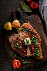 Porterhouse roast steak or Florentine beef steak on a cutting board with seasonings and vegetables....
