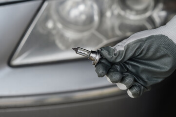 A man in hand holds a halogen low beam lamp next to the headlight of a car,close-up.