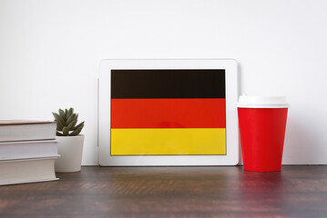 National flag of Germany on the tablet, textbooks, a red cup of hot drink coffee or tea on the...