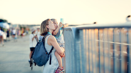 Mom holds her daughter in her arms looking at the fence at a public event, mom and daughter photo...