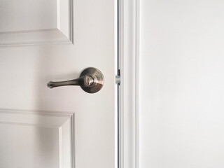 Porte blanche en bois entrouverte. Gros plan sur une poignée de porte argent métallique, loquet, cadrage et mur. Ouverture ou fermeture d'une porte.
