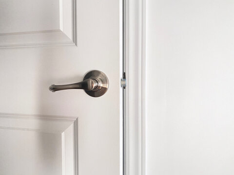 Porte blanche en bois entrouverte. Gros plan sur une poign&eacute;e de porte argent m&eacute;tallique, loquet, cadrage et mur. Ouverture ou fermeture d'une porte.