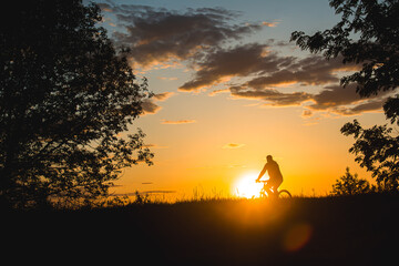 Fototapeta na wymiar A cyclist rides through a field against the backdrop of a beautiful contour sunset light. Beautiful sunset. Photo of nature. Velotheme.