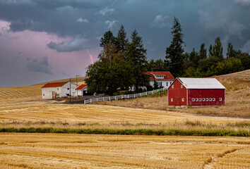 A farm with a red barn in a lightning storm in the fall season in the palouse wheat country in...