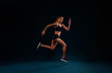 Fototapeta na wymiar Female runner sprinting on black background. Fit woman jumping while exercising in studio.