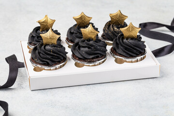 Black cupcakes decorated with a gold star in a box on a light background