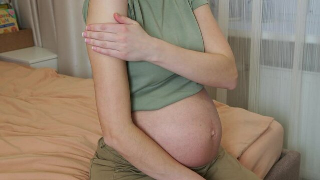 Vaccinated pregnant woman showing at her arm with adhesive tape after vaccine injection and touching belly. Covid vaccination concept. Health care and medicine during pregnancy.